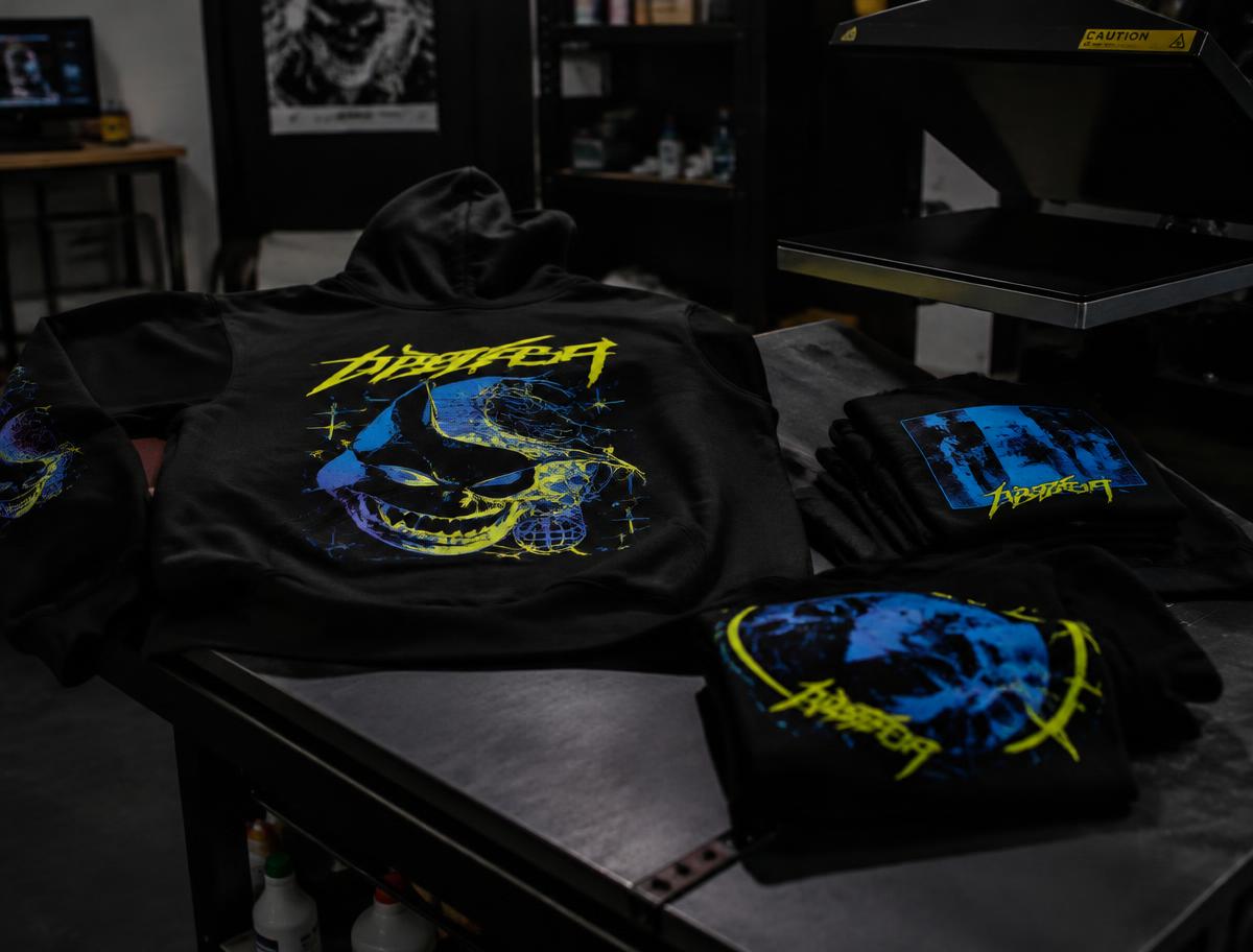 Black hoodie and t-shirts with lime and blue printed graphics on a heat press table